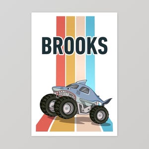 May include: A blue monster truck with a shark fin and teeth, with the name "BROOKS" in black text above it. The truck is on a background of colorful vertical stripes.