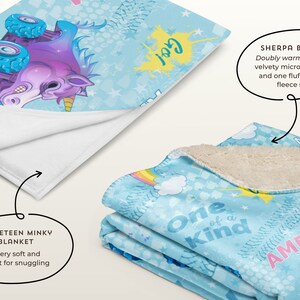 May include: A blue and white sherpa blanket featuring a unicorn design. The blanket has the text "One of a Kind" and "Amelia" on it. The blanket is folded in half, showing the sherpa side.