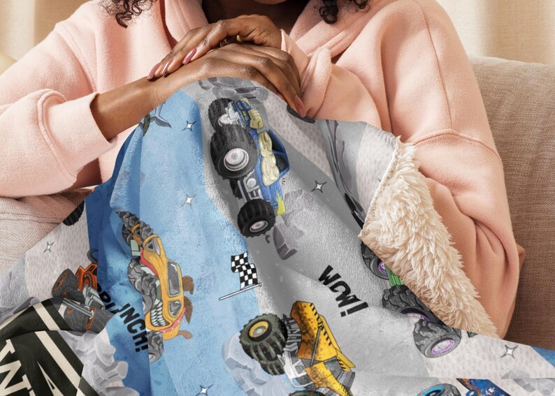 May include: A blue, gray, and white monster truck blanket with a soft, plush sherpa lining. The blanket features colorful monster truck illustrations, a checkered flag, and the word "WOW!"