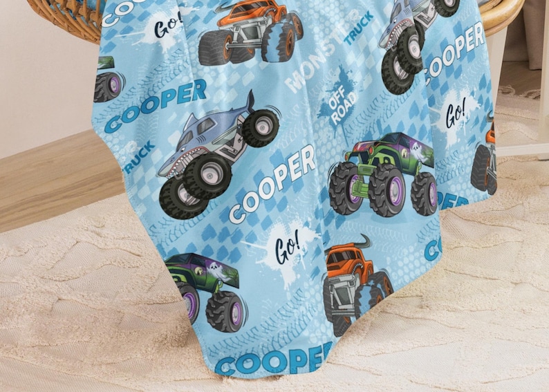 Pu&ograve; includere: Tessuto a tema monster truck blu e bianco con il nome "COOPER" ripetuto su tutto. Il tessuto presenta immagini di monster truck, tra cui uno squalo, un fantasma e un teschio. Il testo "Go!" e "Monster Truck" sono anche inclusi sul tessuto.