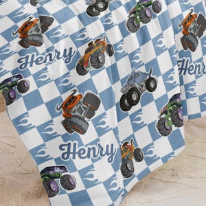 May include: A blue and white checkered baby blanket with a monster truck design and the name "Henry" repeated throughout.