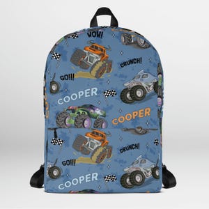 May include: Blue backpack with a monster truck pattern. The backpack has the words "GO!!!", "WOW!" and "CRUNCH!" printed on it. The backpack also has the name "COOPER" printed on it.