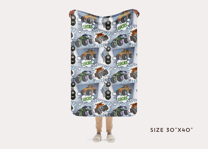 Puede incluir: Una manta de franela azul y blanca con un patr&oacute;n repetido de monster trucks, neum&aacute;ticos y la palabra "Lucas". La manta mide 76 cm por 102 cm.