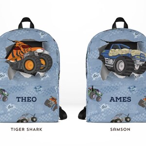 May include: Two blue backpacks with monster truck designs. One features an orange tiger shark truck, the other a blue truck. Each has a name printed on it. The background has a repeating pattern of monster trucks and the words "Go" and "Off Road".