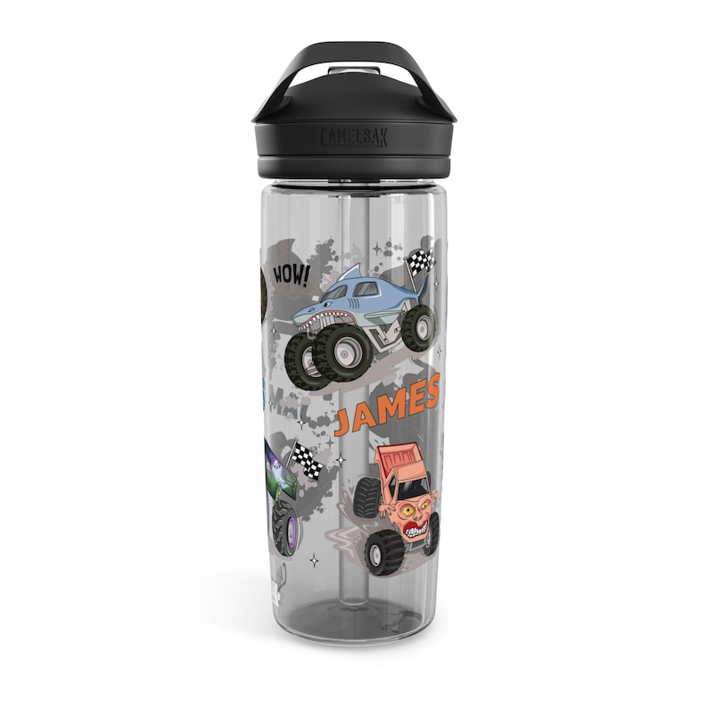 May include: Clear water bottle with a black lid and handle. The bottle features colorful monster truck graphics, including a shark-themed truck and the name "JAMES". The word "WOW!" is also displayed.