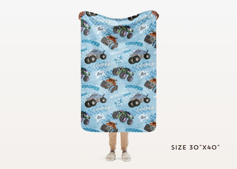 Pu&ograve; includere: Una coperta in pile blu e bianca con un motivo ripetitivo di monster truck. I camion sono blu e grigi con ruote nere e le parole "COOPER" e "Monster Truck" sono stampate sulla coperta. La coperta misura 76 cm per 102 cm.