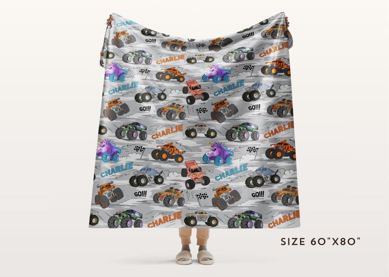 May include: A grey blanket featuring a pattern of colourful cartoon monster trucks. The blanket has the name "Charlie" and the word "GO!!!" printed on it. The blanket measures 152cm x 203cm.