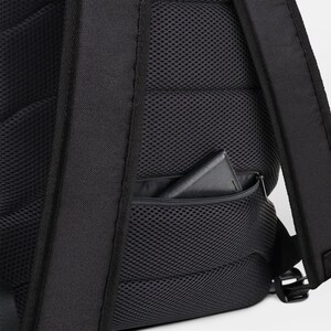 May include: Black backpack with a zippered pocket on the side. The pocket has a black mesh lining and a black phone or wallet inside.