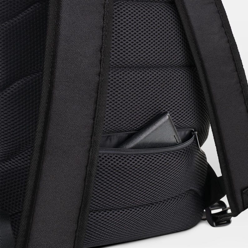May include: Black backpack with a zippered pocket on the side. The pocket has a black mesh lining and a black phone or wallet inside.