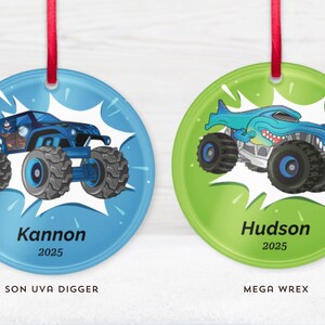 May include: Two round Christmas ornaments with red ribbon hangers. One is blue with a monster truck design and the name "Kannon" and the year "2025". The other is green with a shark-themed monster truck and the name "Hudson" and the year "2025".