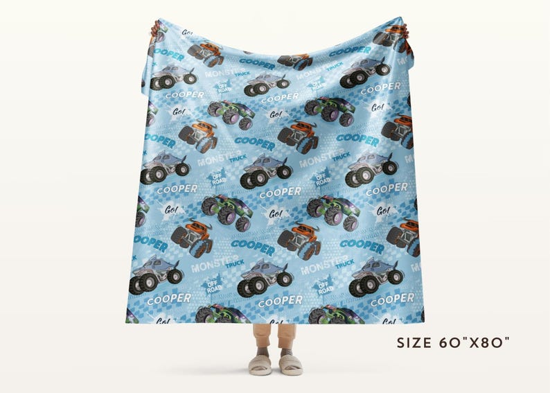 Pu&ograve; includere: Una coperta in pile blu e bianca con un motivo ripetitivo di monster truck. I camion sono verdi, neri e arancioni con il nome "Cooper" stampato su ogni camion. La coperta misura 152 cm per 203 cm.
