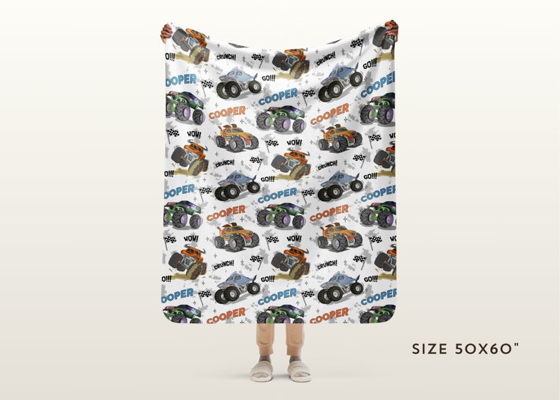 May include: A white fleece blanket featuring a repeating pattern of monster trucks in various colours, including orange, blue, and green. The trucks have large wheels and are driving on a white background with black tyre tracks. The words "COOPER", "GO!!!", "WOW", "CRUNCH", and "O!!!" are printed on the blanket.