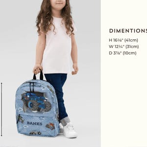 May include: A light blue backpack with a monster truck design. The backpack is 16 5/8" (41cm) high, 12 1/4" (31cm) wide, and 3 7/8" (10cm) deep. The word "BANKS" is printed on the backpack.