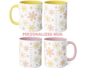 Könnte beinhalten: Eine weiße Keramiktasse mit rosafarbenem Rand und Henkel. Die Tasse hat ein Blumenmuster mit rosa und gelben Blumen. Der Text "JENNIFER" ist vertikal auf die Tasse gedruckt.