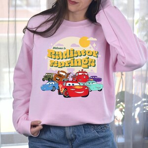 a woman wearing a pink sweatshirt with cars on it