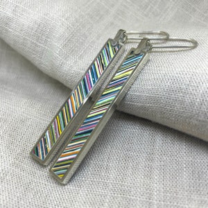 May include: A pair of silver dangle earrings with colourful striped enamel. The stripes are in various colours, including black, white, yellow, green, blue, and red.
