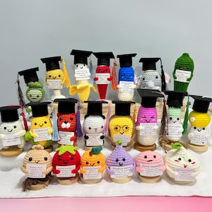 Puede incluir: Una colección de figuras de ganchillo con temática de alimentos, cada una con un gorro de graduación y un pequeño letrero. Las figuras incluyen un plátano, un pimiento y una cebolla, entre otros. La paleta de colores es vibrante, con varios tonos de amarillo, rojo y verde.