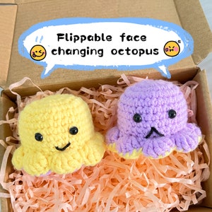 May include: Two crocheted octopus toys with flippable faces. One is yellow with a smiling face, the other is purple with a frowning face. The toys are in a cardboard box with pink paper filler. Text on the box says "Flippable face changing octopus."