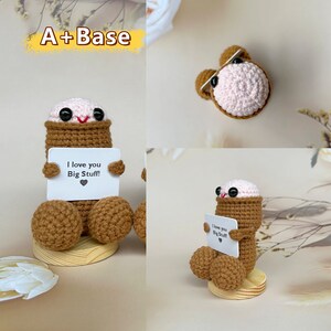 Puede incluir: Una figura de crochet marr&oacute;n y rosa sosteniendo una tarjeta que dice "Te quiero Mucho!" La figura est&aacute; sentada sobre una base de madera.