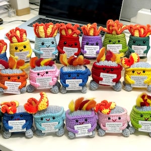 May include: A collection of colorful, crocheted "Emotional Support Dumpster Fire" figurines. Each has a smiling face, flames, and a sign that reads "It's fine. I'm fine. Everything is fine!" in various colors.