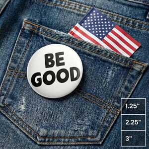 Pode incluir: Um botão branco com as palavras "BE GOOD" em letras pretas em negrito está em um bolso de jeans azul. Uma bandeira americana também está no bolso. O botão tem 3,18 cm de diâmetro. O bolso está em um par de jeans.