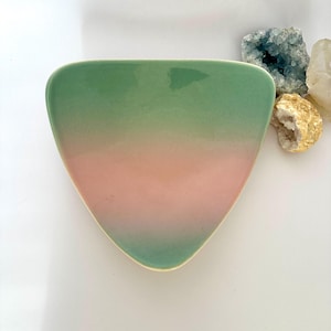 May include: A triangular ceramic dish with a gradient of green to pink hues. The dish has a smooth, glossy finish and a slightly raised edge. Decorative crystals are in the background.