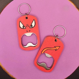 May include: Two red wooden bottle opener keychains. One features a face with angry eyes and a wide open mouth. The other has a curved arrow design. Both have a silver bottle opener and a silver key ring.