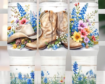 May include: A set of three white insulated tumblers with a floral and Western theme. The design features a cowboy hat, tan cowboy boots, and colorful flowers against a white wood background. The bottom of the tumblers have a floral design.