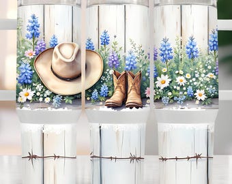 May include: Three white tumblers with a rustic woodgrain design. Each tumbler features a different scene: a cowboy hat, a pair of brown cowboy boots, and a field of blue and white wildflowers. The tumblers have a white lace trim and a barbed wire design at the bottom.