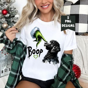 K&ouml;nnte beinhalten: Wei&szlig;es T-Shirt mit einer gr&uuml;nen Grinch-Hand, die sich nach einem schwarzen Hund ausstreckt, mit dem Wort "Boop" und einem gr&uuml;nen Herzen darunter.