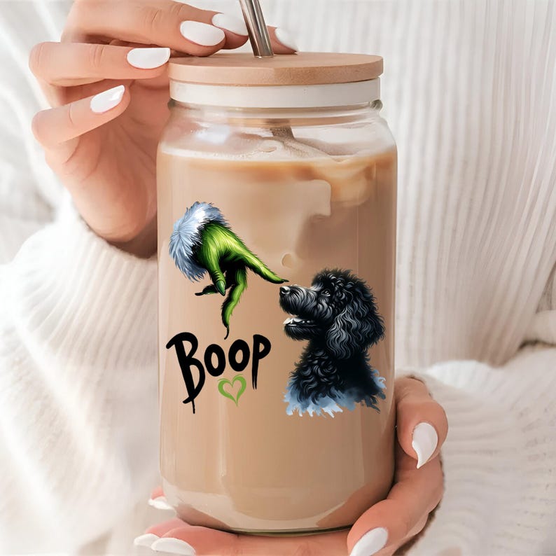 K&ouml;nnte beinhalten: Ein Glasgef&auml;&szlig; mit einem Holzdeckel und einem Strohhalm. Das Gef&auml;&szlig; ist mit Eiskaffee gef&uuml;llt und hat eine gr&uuml;ne Hand und einen schwarzen Hund mit dem Wort "Boop" und einem Herz darauf gedruckt.