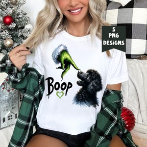 K&ouml;nnte beinhalten: Wei&szlig;es T-Shirt mit einer gr&uuml;nen Grinch-Hand, die sich nach einem schwarzen Pudel mit dem Text "Boop" und einem gr&uuml;nen Herzen ausstreckt.