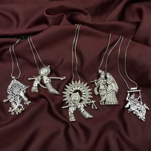May include: Six silver necklaces with different pendants featuring Hindu deities. The pendants are detailed and intricate, with designs of Krishna and Radha, a peacock feather, and other religious symbols.