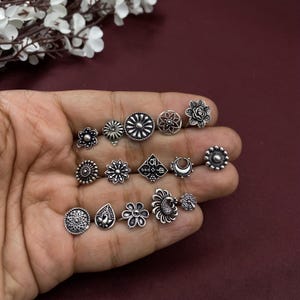 Pu&ograve; includere: Un set di 14 anelli per il naso in argento con vari disegni, tra cui fiori, lune e forme geometriche.