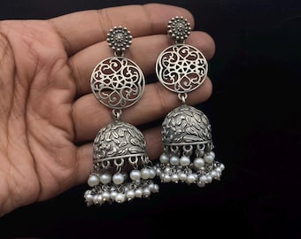 May include: Silver earrings with a circular filigree design and a bell-shaped dangle accented with white pearls.
