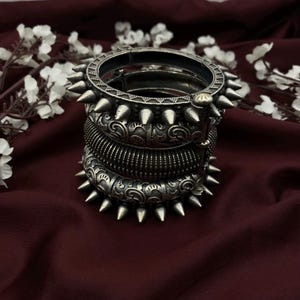 Puede incluir: Un conjunto de cuatro brazaletes de plata con diseños intrincados y bordes puntiagudos. Los brazaletes están apilados uno encima del otro y tienen un acabado plateado.