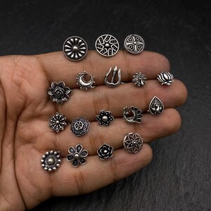 Pu&ograve; includere: Un set di 16 anelli per il naso in argento con vari disegni, tra cui fiori, pavoni, lune e forme geometriche.