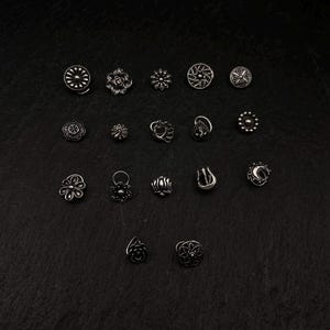 Pu&ograve; includere: Una collezione di 18 anelli per il naso in argento con vari disegni, tra cui fiori, pavoni e forme geometriche.