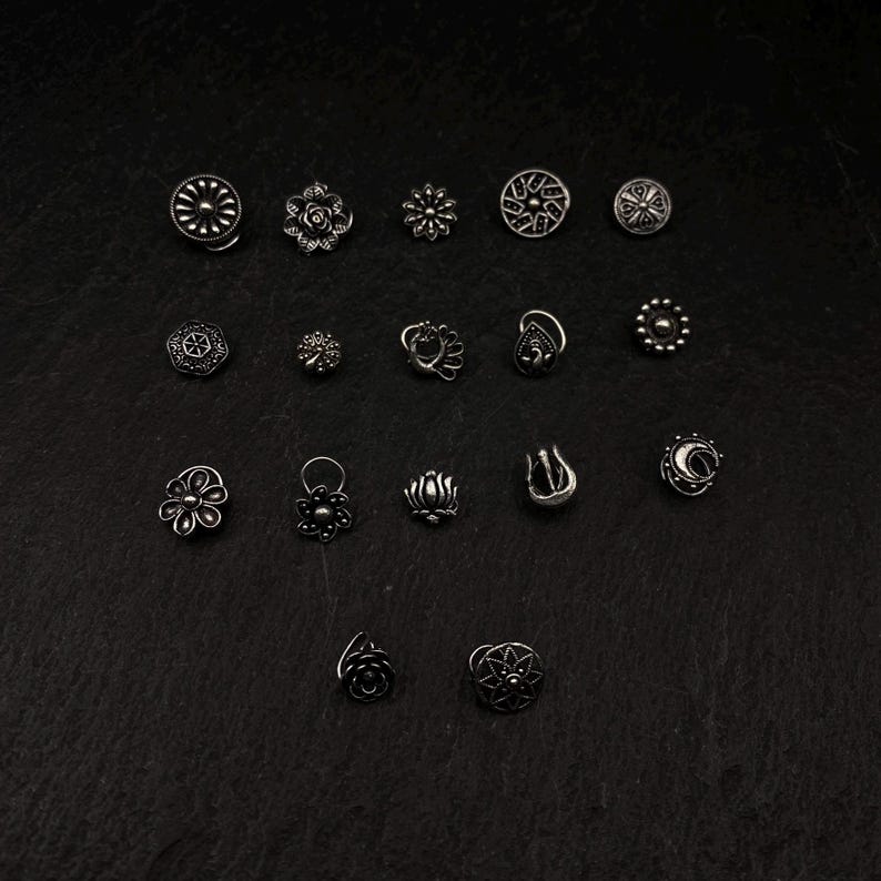 Pu&ograve; includere: Una collezione di 18 anelli per il naso in argento con vari disegni, tra cui fiori, pavoni e forme geometriche.