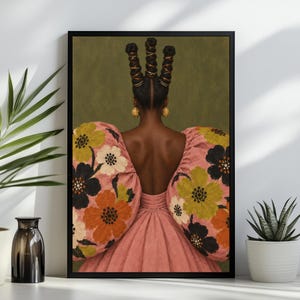 May include: A framed wall art print depicting the back view of a person with three tall, wrapped hair buns and gold earrings. The person wears a pink dress with large, puffed sleeves featuring a bold floral pattern in orange, white, and black.