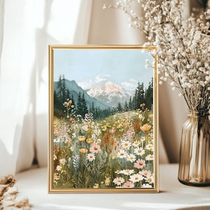 May include: A rectangular wall art print in a thin gold frame depicting a mountain landscape. The scene features a snow-capped mountain peak, dark green pine trees, and a vibrant foreground filled with various wildflowers in shades of white, pink, and yellow.