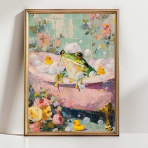 May include: A framed painting depicts a green frog in a pink bathtub filled with bubbles. Yellow rubber duckies float nearby. The background features floral patterns and a light blue tiled wall. The artwork has a gold frame.