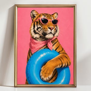 Könnte beinhalten: Ein gerahmter Kunstdruck, der einen Tiger mit einer rosa Sonnenbrille und einem rosa Halstuch zeigt. Der Tiger hält einen leuchtend blauen aufblasbaren Schwimmring vor einem einfarbigen, kräftigen rosa Hintergrund. Der Rahmen ist goldfarben.