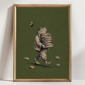 May include: A framed wall art print featuring a black ink illustration of a frog wearing a jacket and trousers, walking while carrying a stack of five books. A small bee flies above the frog, and four fallen leaves are scattered on the ground.