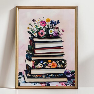 May include: A framed art print featuring a stack of books topped with a vibrant bouquet of flowers. The books have white pages and colorful spines. The background is a soft pink with brushstrokes.