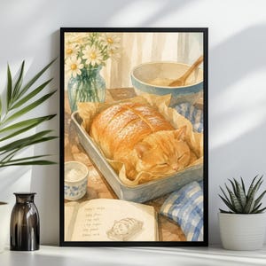 May include: A framed watercolor illustration of an orange tabby cat curled up inside a rectangular baking pan, resembling a loaf of bread. Beside it sits a glass vase with white daisies, a mixing bowl with a wooden spoon, and a recipe book.