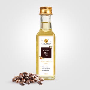 Op de afbeelding: Een heldere glazen fles ricinusolie voor haar met een gouden dop, met het opschrift "Castor Hair Oil". Naast de fles ligt een stapel bruine ricinusbonen. Het etiket vermeldt ook "Paraben & Mineral Oil Free".