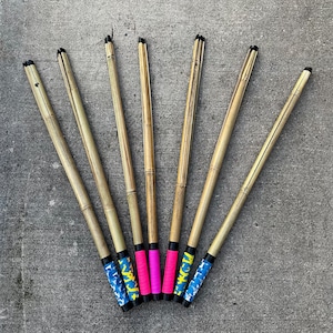 May include: Seven wooden sticks with colourful patterned tape wrapped around the ends. The sticks are arranged in a fan shape on a grey concrete surface.