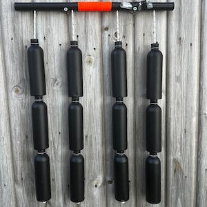 May include: A black metal bar with an orange stripe hangs from a wooden wall. Six black plastic bottles are suspended from the bar by ropes.