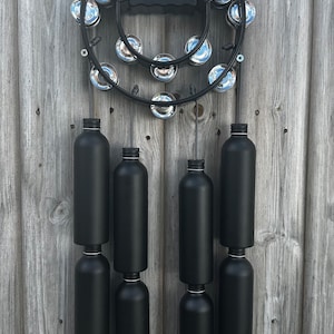 May include: A black metal tambourine with silver jingle bells and eight black painted metal tubes hanging from it.